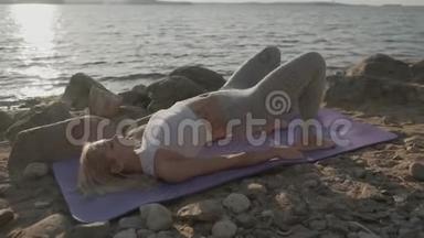 那个美丽的运动女子在海滨做早操。 海滩和日出的背景